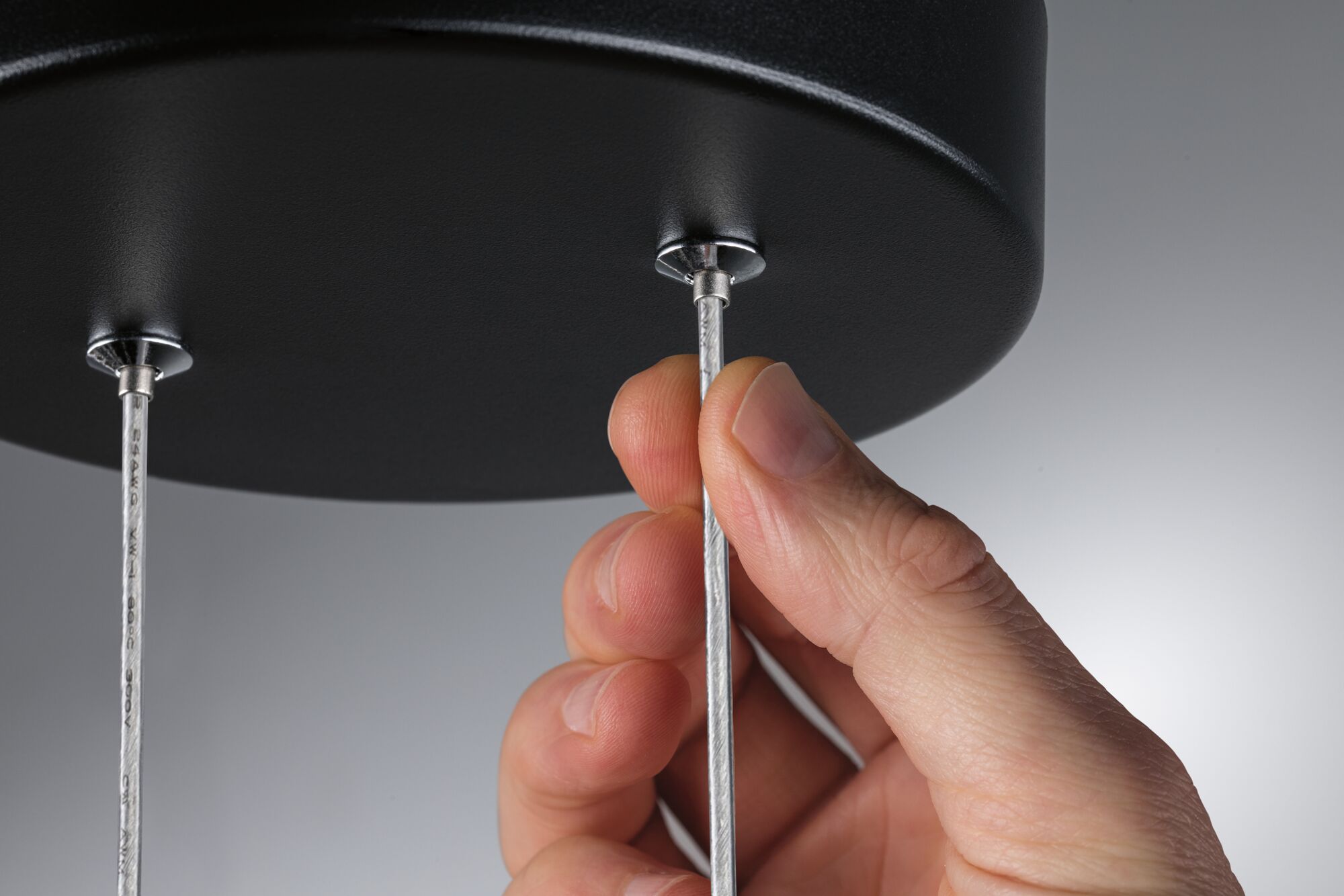 Hand holding silver cable on black round metal ceiling light for modern indoor lighting fixture