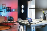 Salon moderne avec fauteuil gris, lampe sur pied, tapis rond et éclairage mural LED aux tons bleu et rouge.