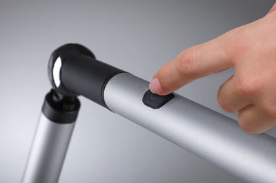 Hand pressing black switch on silver aluminum LED reading lamp with flexible joint for office use.
