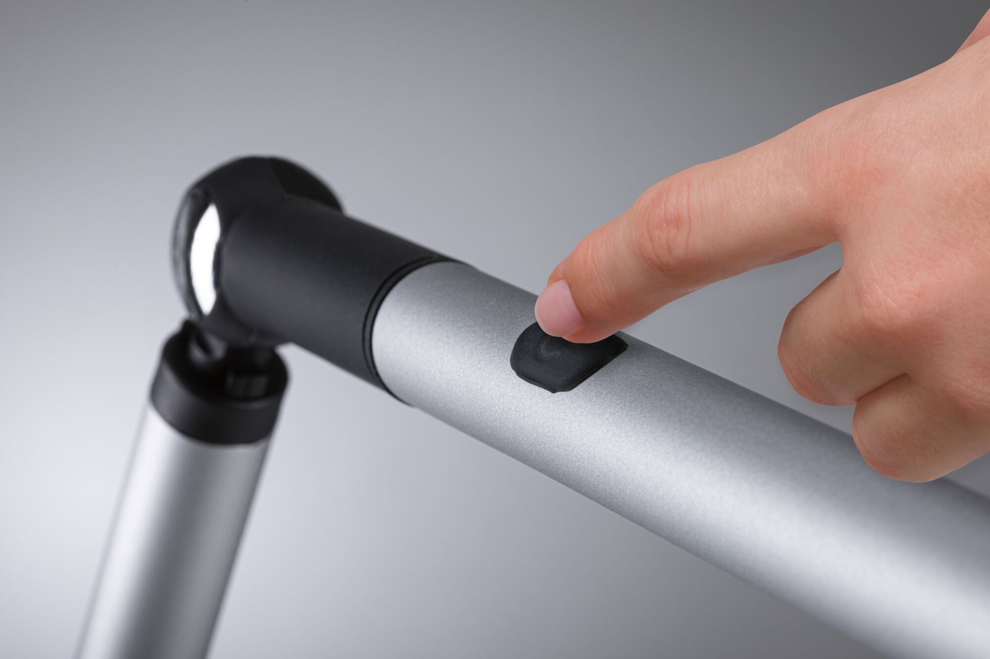 Main appuyant sur interrupteur noir d'une lampe de lecture LED en aluminium argenté avec articulation flexible.