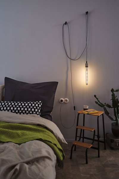 Chambre avec tube LED suspendu blanc chaud, marchepied en bois et couverture verte pour une ambiance chaleureuse