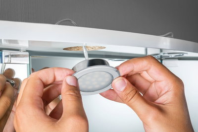 Hände montieren runden LED-Einbaustrahler in weißem Möbel mit Holzplatte, LED-Beleuchtung