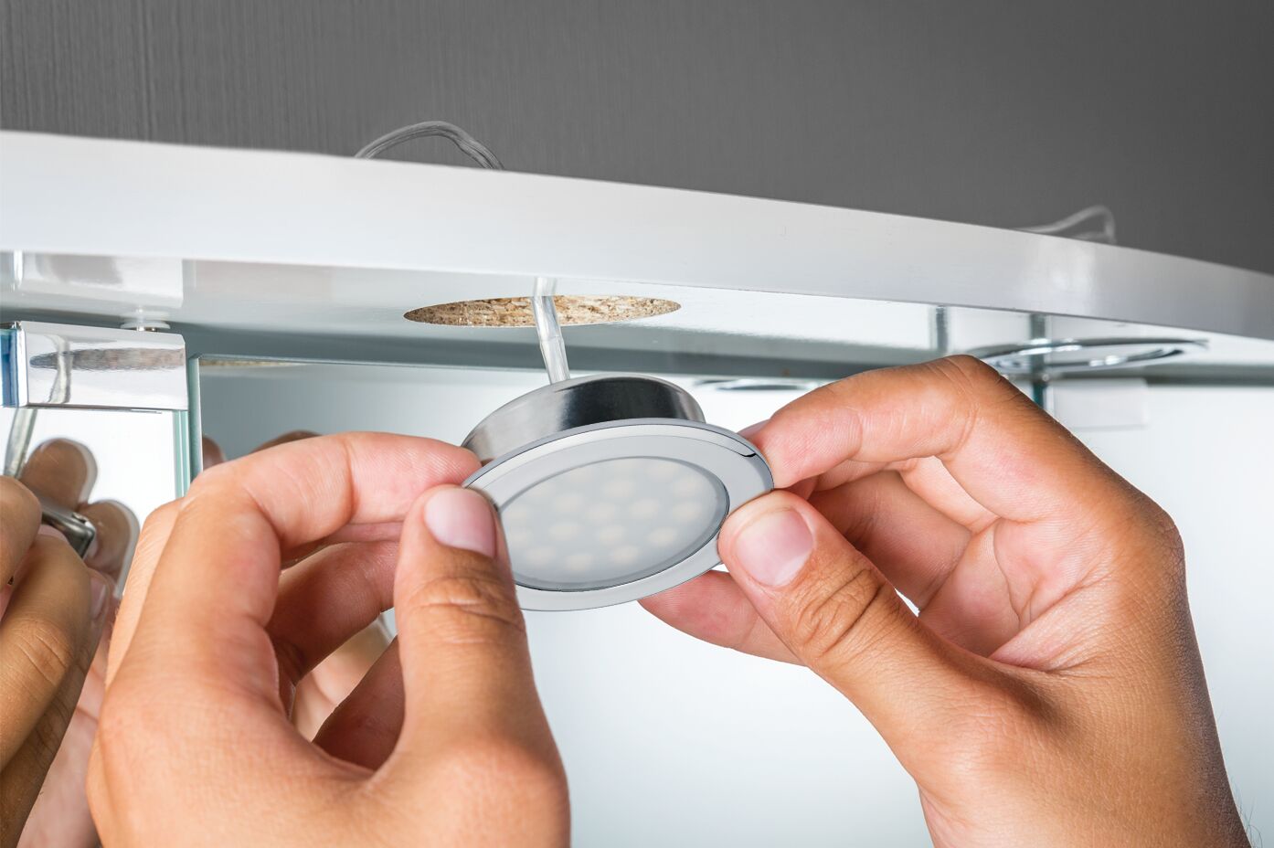 Hands installing round white LED recessed spotlight in furniture with wood panel, LED lighting