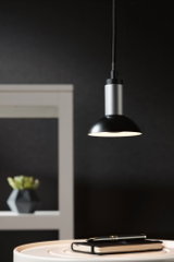 Moderne schwarze und silberne Pendelleuchte aus Metall über einem Tisch mit Notizbuch und Stift