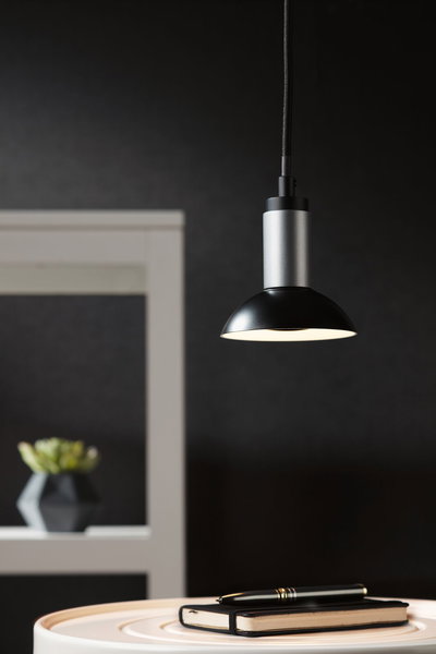 Modern black and silver metal pendant lamp above table with notebook and pen, interior lighting