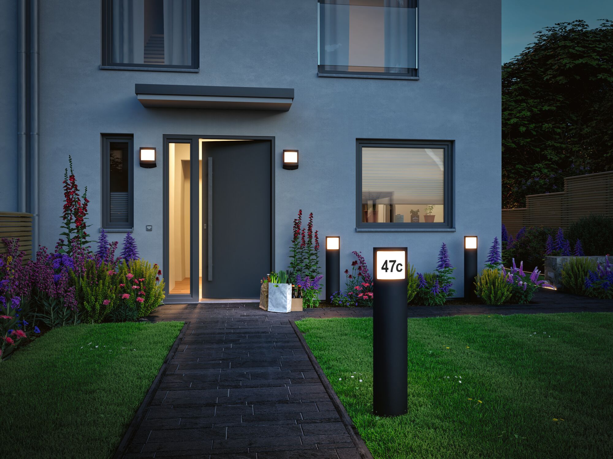 Maison moderne avec façade grise, porte noire et lampes extérieures en métal éclairant l'allée du jardin