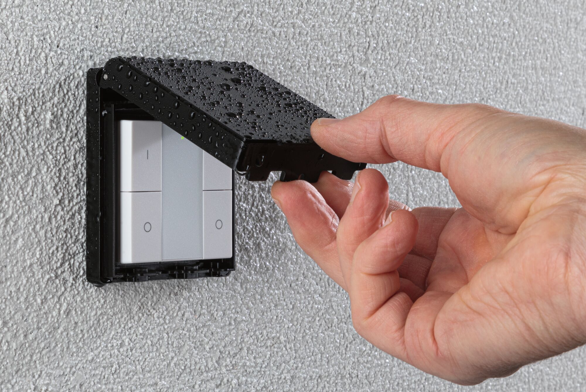 Hand tilt zwarte waterdichte kap van witte plastic wandlichtschakelaar op gestructureerde muur.