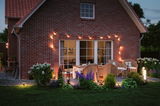Cozy patio with warm white LED garden lights and rattan furniture in front of red brick house.