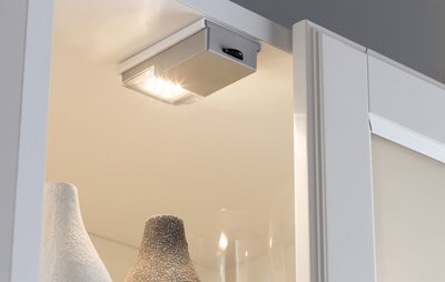 Compact silver LED under-cabinet light with warm white illumination for furniture and display cases.