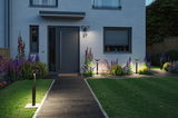 Moderne zwarte LED-buitenlampen verlichten pad en huisgevel met tuinplanten bij schemering