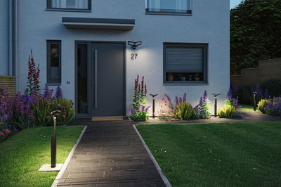 Moderne zwarte LED-buitenlampen verlichten pad en huisgevel met tuinplanten bij schemering
