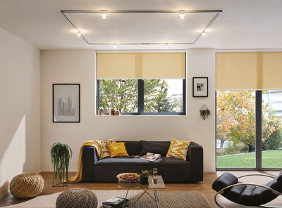 Modernes Wohnzimmer mit schwarzem Sofa, gelben Kissen und Decken, Glas-Couchtisch und gelben Rollos.