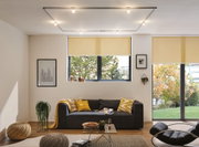 Modernes Wohnzimmer mit schwarzem Sofa, gelben Kissen und Deckenleuchte mit LED-Spots an der Decke