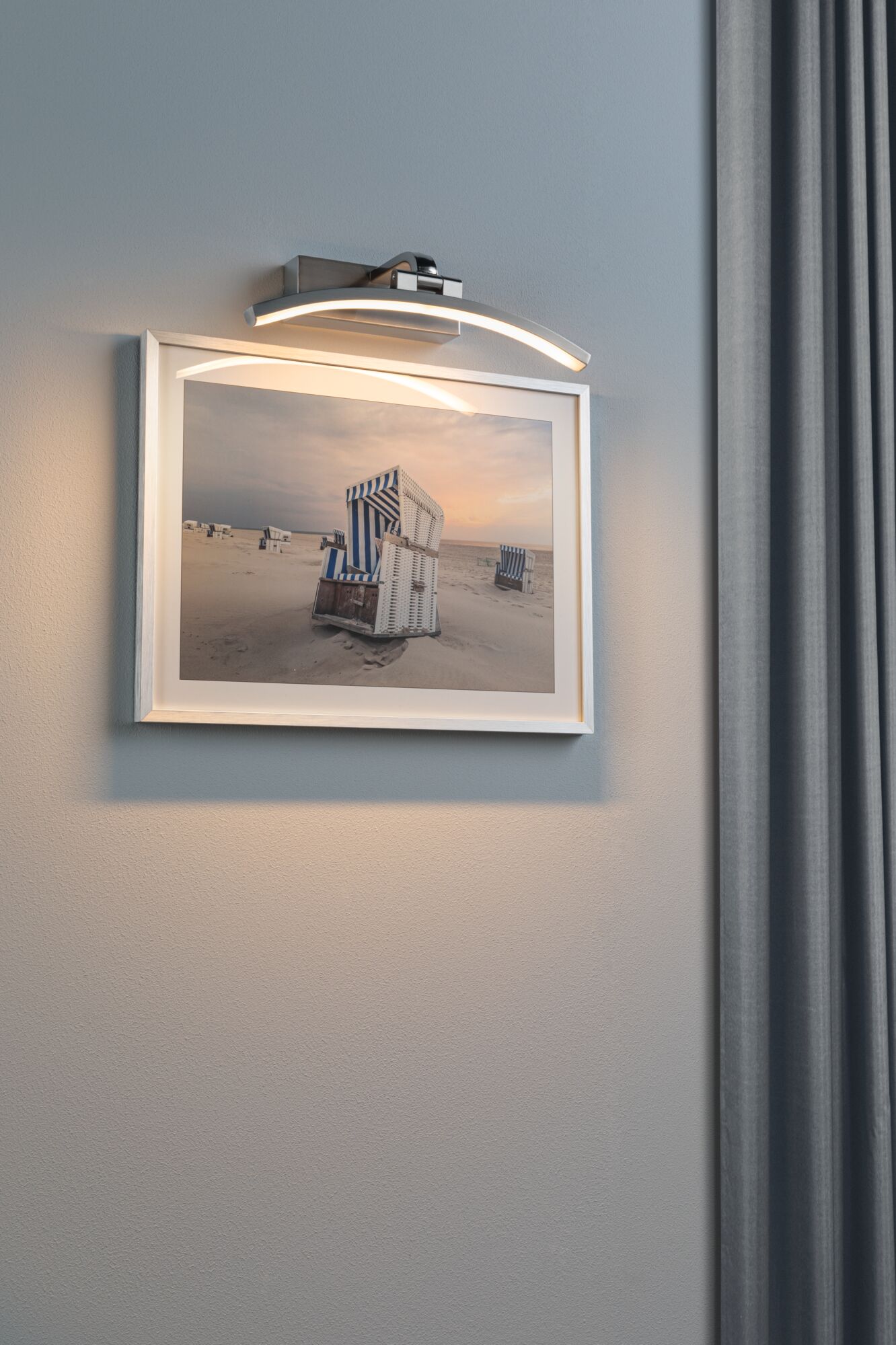 Moderner LED-Bilderleuchter in gebürstetem Metall mit warmweißem Licht an grauer Wand.
