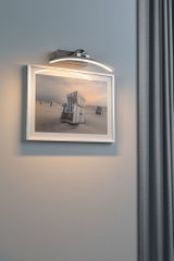 Moderner LED-Bilderleuchter in gebürstetem Metall mit warmweißem Licht an grauer Wand.