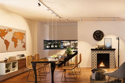 Modern dining room with black wooden table, rattan chairs, and Paulmann URail silver track lighting system.