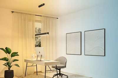 Modern office with light wood desk, grey swivel chair, and black LED pendant light