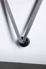 Black metal wall hook with grey fabric strap on white wall for modern interior design