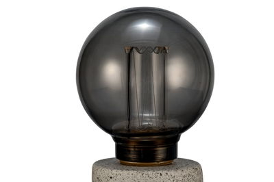Runde Rauchglas-Glühbirne mit sichtbarem Filament auf grauem Steinsockel für dekorative Beleuchtung.
