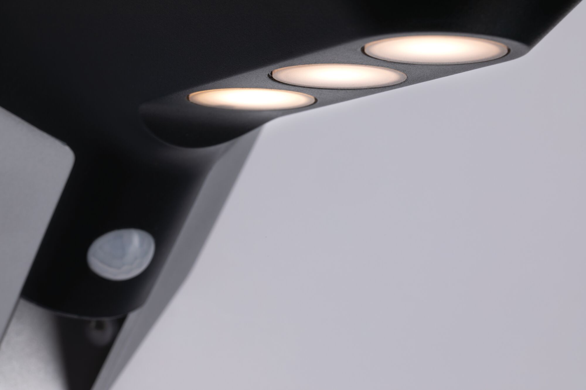 Applique extérieure noire en métal avec trois LED blanc chaud et détecteur de mouvement intégré.