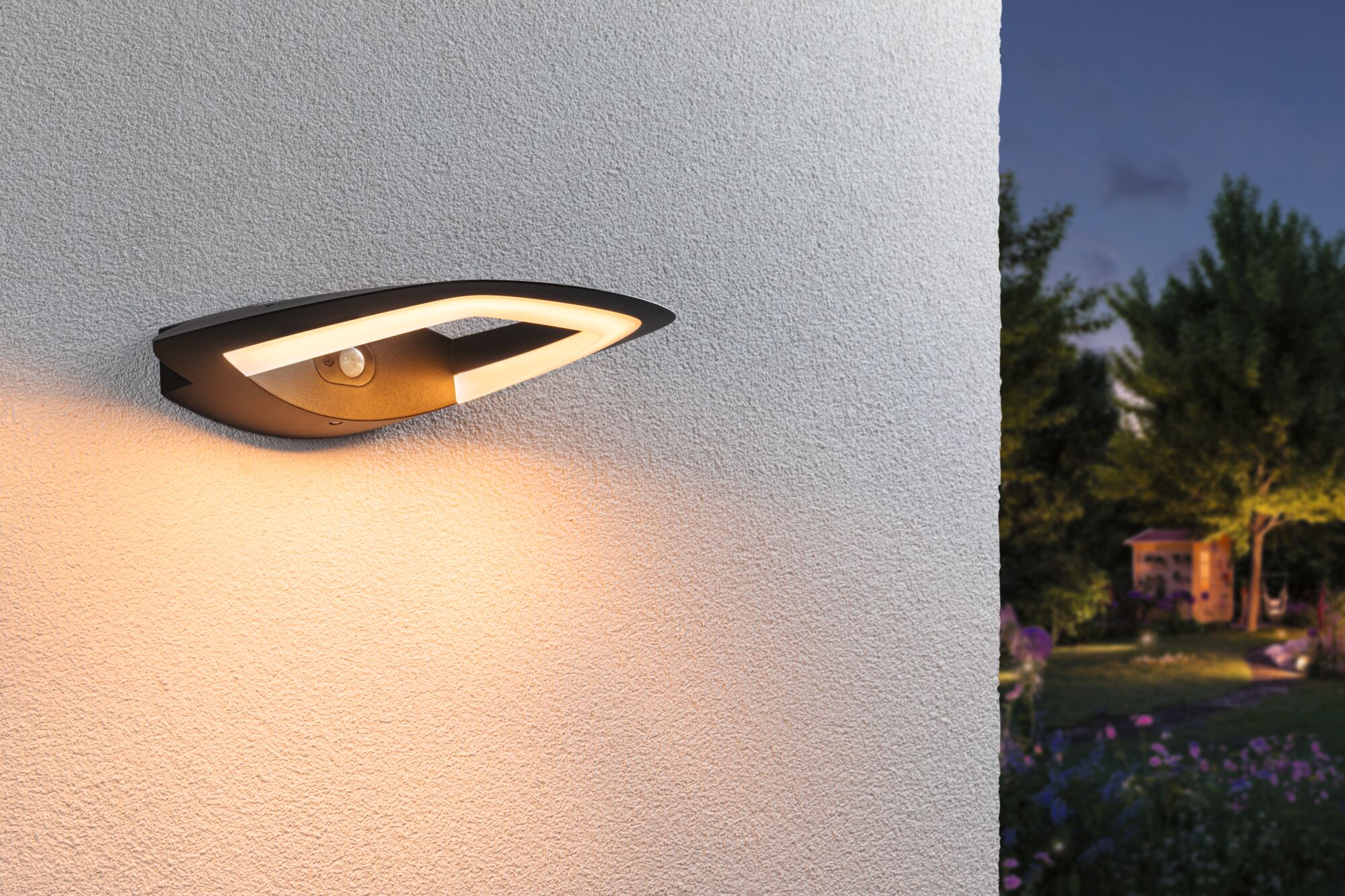 Moderne schwarze LED-Außenwandleuchte mit warmweißem Licht und Bewegungssensor an weißer Wand.