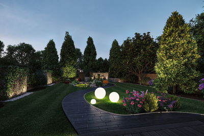 Garden path with black tiles and three white globe lights on green lawn at dusk