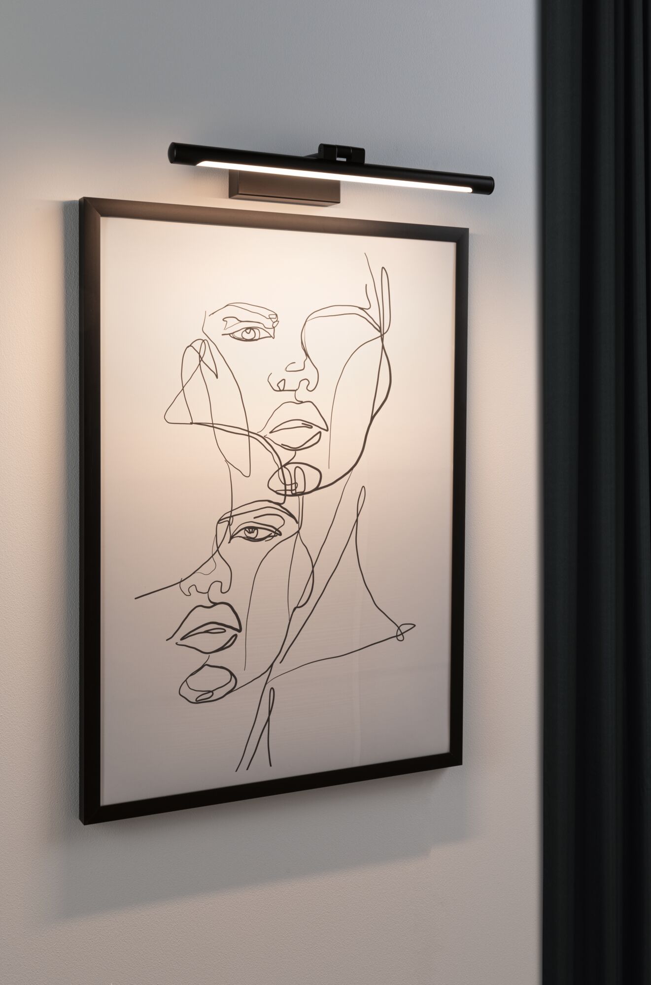 Schwarze LED-Bilderleuchte an Wand beleuchtet minimalistisches Kunstbild mit Liniengesichtern.