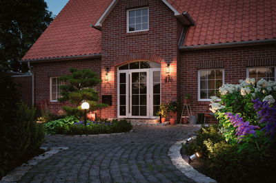 Entrée éclairée d'une maison en briques rouges avec lampes de jardin et porte blanche au crépuscule