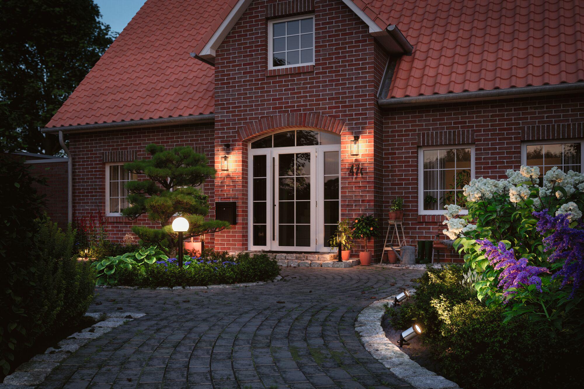 Beleuchteter Eingangsbereich eines roten Backsteinhauses mit Gartenleuchten und weißer Tür im Abendlicht