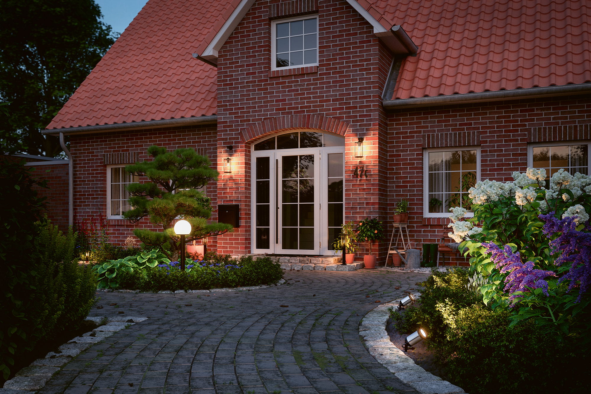 Entrée éclairée d'une maison en briques rouges avec lampes de jardin et porte blanche au crépuscule