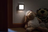 Veilleuse LED blanche en plastique fixée au mur près de peluches pour un éclairage doux dans la chambre d'enfant