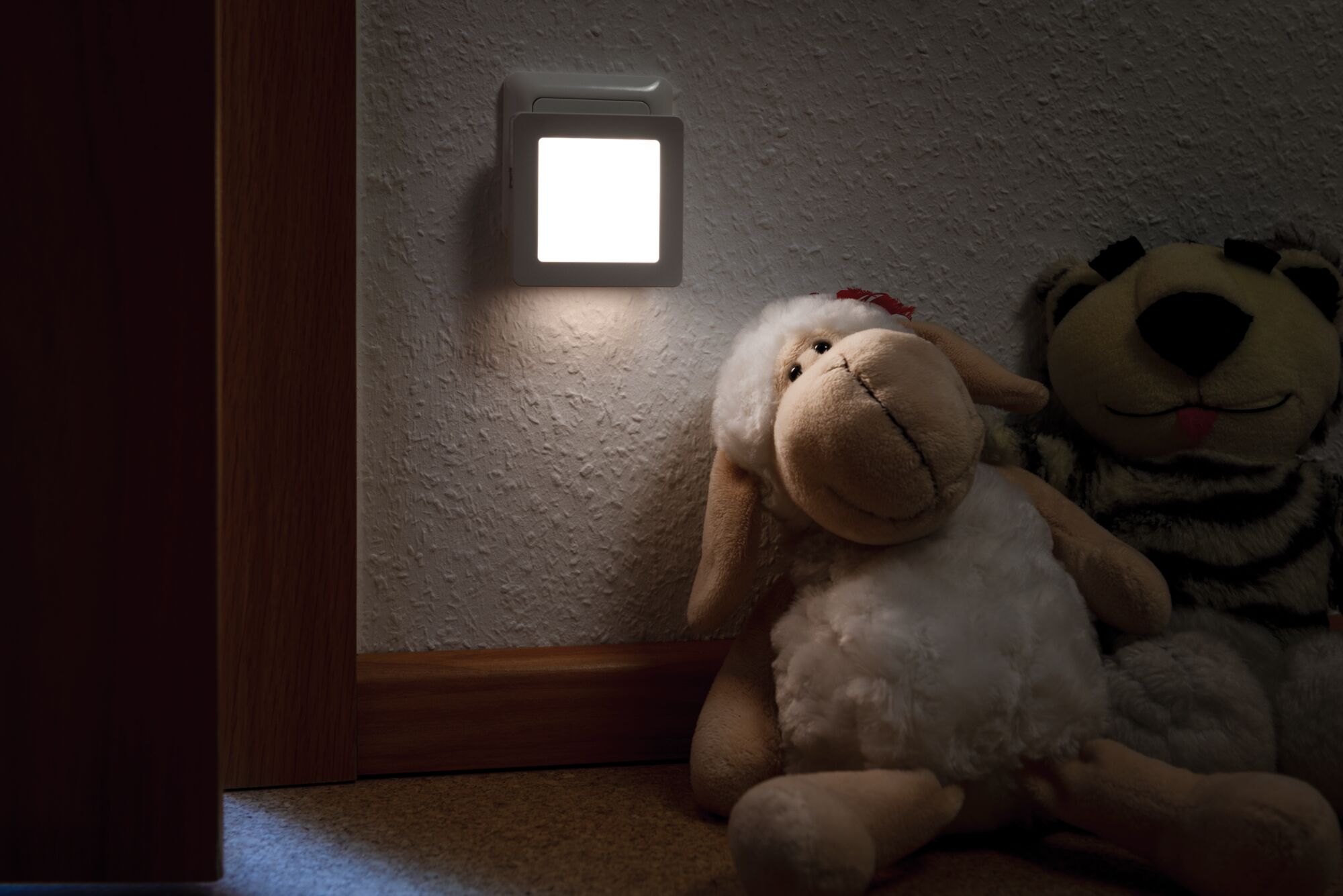 Weißes LED-Nachtlicht aus Kunststoff an Wand neben Kuscheltieren für sanfte Beleuchtung im Kinderzimmer