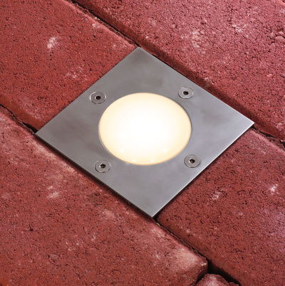 Recessed stainless steel LED floor light with warm white glow in red paving stone