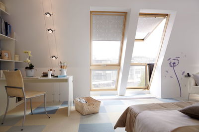 Modernes Dachzimmer mit Holzfenstern, gemusterten Rollos und Kabelstrahlern an der Decke für Wohnraumbeleuchtung