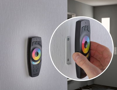 Zwarte LED-afstandsbediening met kleurenwiel aan witte muur gemonteerd, hand die deze eraf haalt, lichtbediening