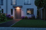 Porte d'entrée grise moderne avec applique murale LED blanc chaud au-dessus dans un jardin.