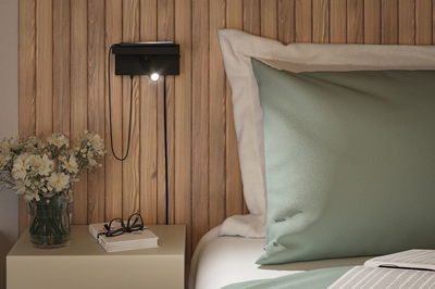 Schwarze LED-Wandleuchte mit flexiblem Lesearm an Holzwand neben Bett mit grünem Kissen und Nachttisch.