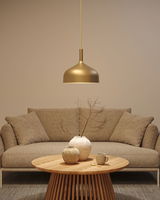 Gouden metalen hanglamp boven ronde houten tafel met keramische vazen en beige bank in woonkamer