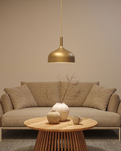 Gold metal pendant lamp above round wooden table with ceramic vases and beige sofa in living room