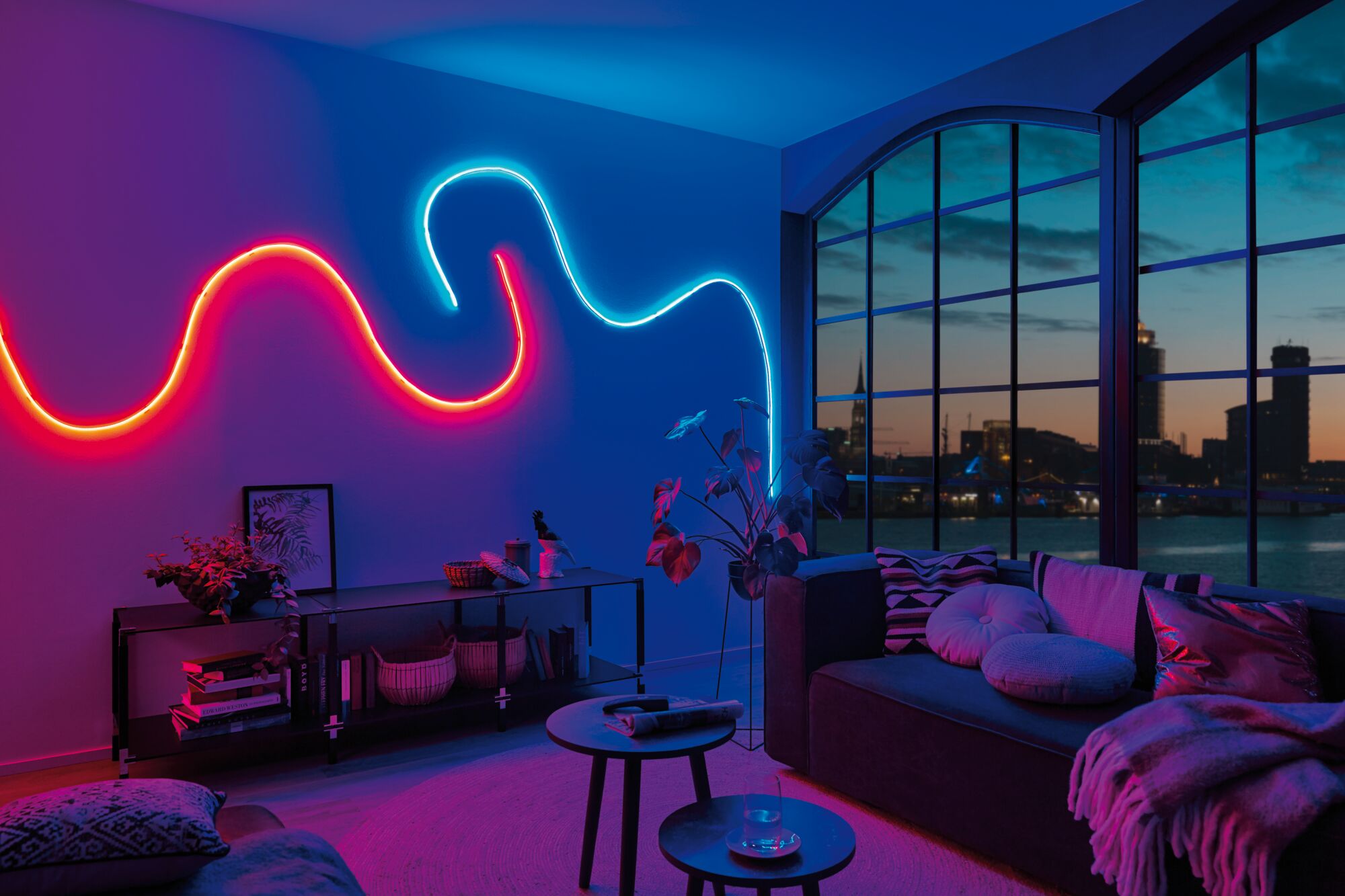 Wohnzimmer mit MaxLED Flow RGB LED-Lichtschlauch in Rot und Blau an der Wand, moderne Ambientebeleuchtung.