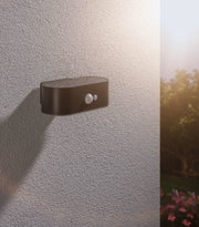 Schwarze Außenwandleuchte aus Metall mit Bewegungsmelder an strukturierter Wand im Gartenbereich