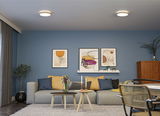Modernes Wohnzimmer mit blauer Wand, grauem Sofa, bunten Kissen und zwei runden Deckenleuchten.