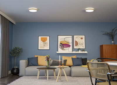 Modernes Wohnzimmer mit blauer Wand, grauem Sofa, bunten Kissen und zwei runden Deckenleuchten.