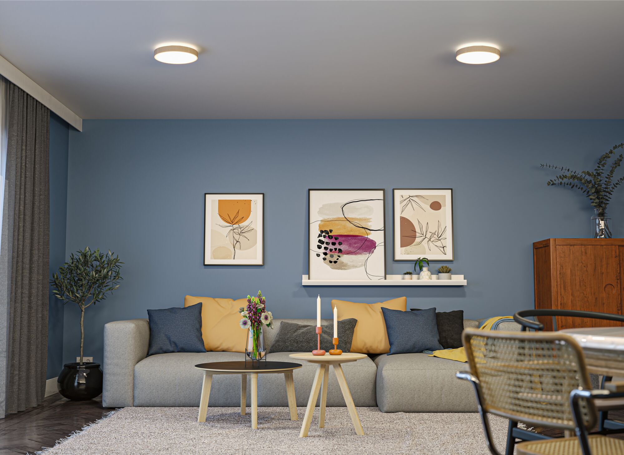 Moderne woonkamer met blauwe muur, grijze bank, kleurrijke kussens en twee ronde plafondlampen.