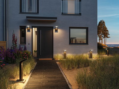 Moderne Außenbeleuchtung mit schwarzen LED-Wegeleuchten und Wandlampen an Hausfassade bei Dämmerung.