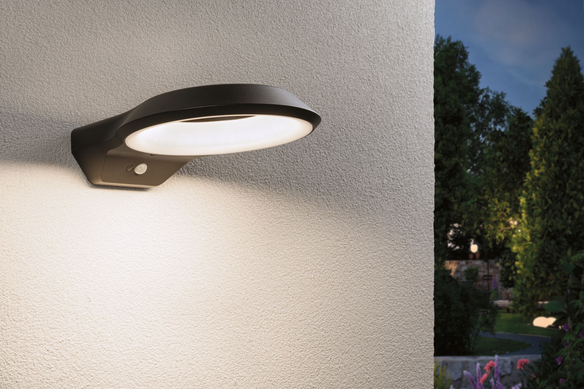 Schwarze LED-Außenwandleuchte aus Metall mit Bewegungsmelder an weißer Wand im Garten.