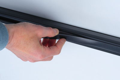 Hand holding black rubber sealing strip on smooth white surface for sealing and protection