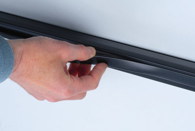 Hand hält schwarzen Gummidichtungsstreifen an glatter weißer Oberfläche für Abdichtung und Schutz