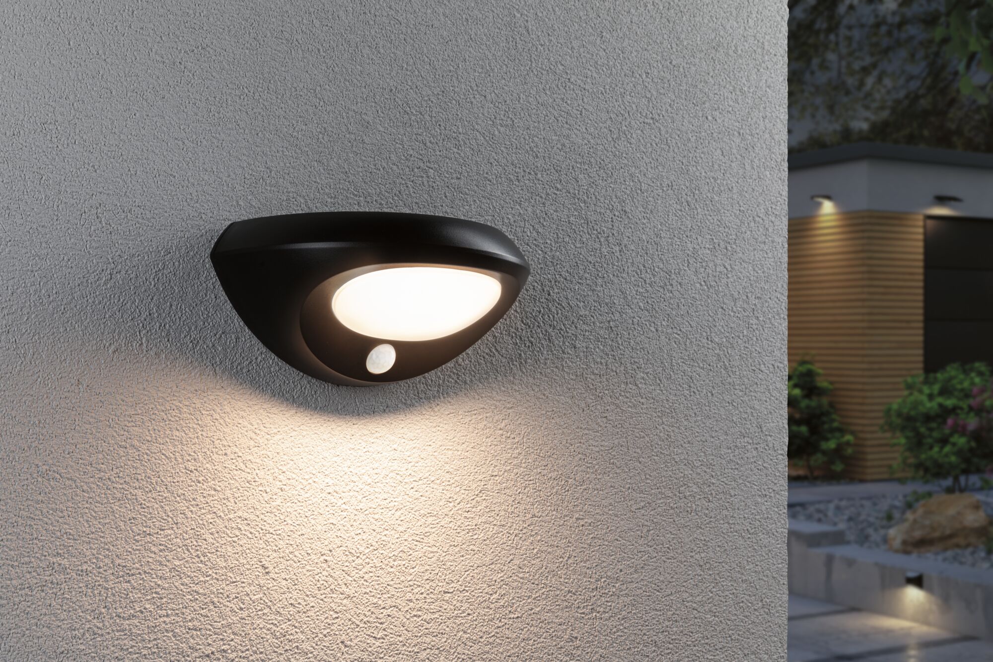 Black outdoor wall light with motion sensor on grey wall, warm white light for garden illumination