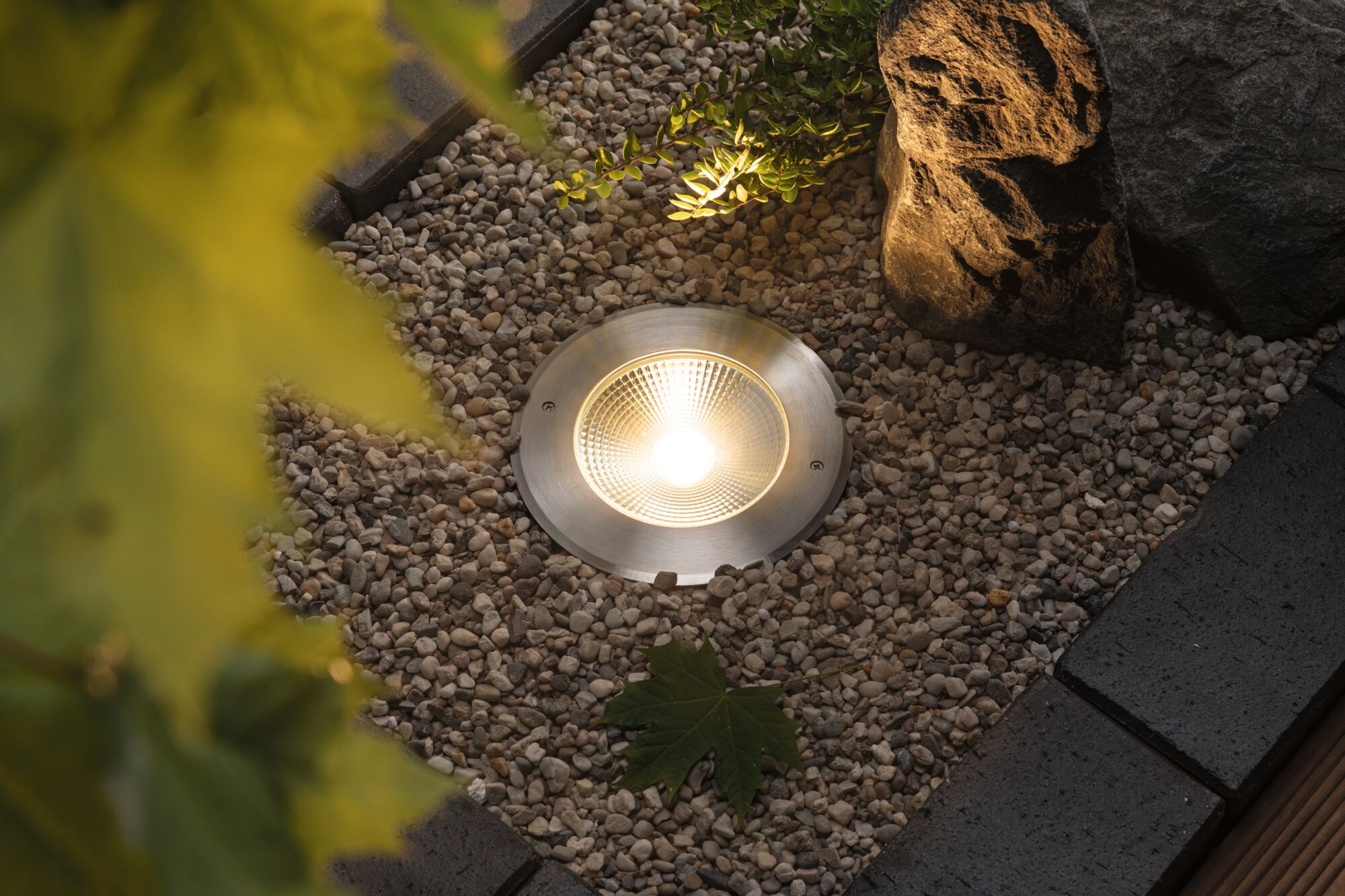 Erdstrahler aus gebürstetem Edelstahl mit warmweißem LED-Licht im Kiesbeet für Gartenbeleuchtung
